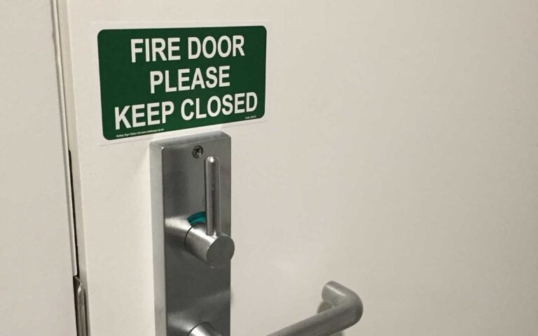 A "fire door please keep closed" sign on a door for building code compliance.